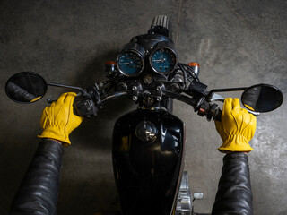 Close-up of biker in yellow leather gloves holding motorcycle handlebars. Top view