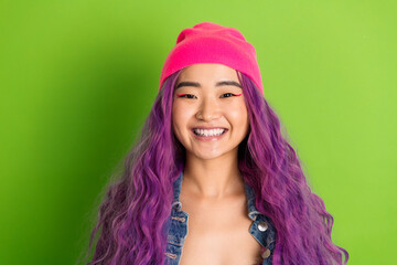Smiling young woman with vibrant purple hair wearing a beanie and denim jacket on a striking green...