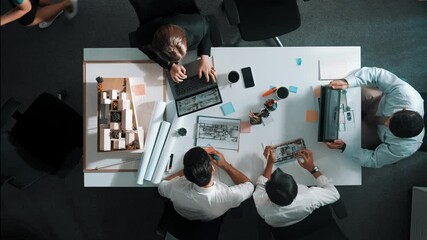 Top view of smart architect engineer writing at blueprint while sitting at meeting table with house model and laptop. Skilled manager working and taking about about building structure. Alimentation.