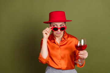 Young stylish woman in vibrant clothing holding a wine glass while expressing a unique gesture...