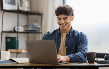 Happy Arabic Man Using Laptop Typing And Browsing Internet Sitting At Table In Office. Young Businessman Working Online On Computer At Modern Workplace. Entrepreneurship Concept