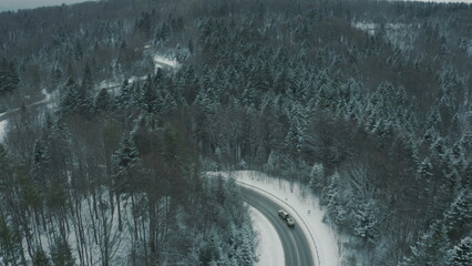 Aerial view of a winding snowy mountain road cutting through a dense winter forest. Mountain road...