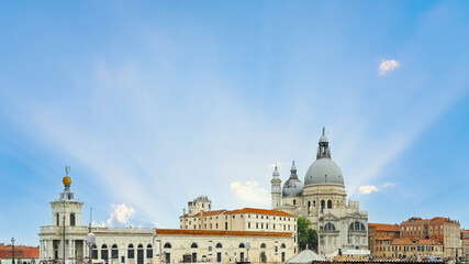 Obraz premium Sun rays illuminate the iconic Santa Maria della Salute basilica and historic Venetian architecture under a beautiful blue sky, a famous travel destination and landmark in Venice, Italy