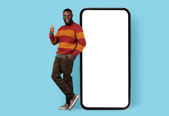 Online Promo. Joyful Black Man Standing Near Big Blank Smartphone And Showing Thumb Up, Cheerful...