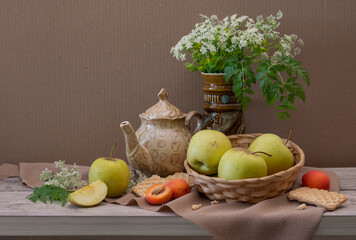 Still life: a bouquet of small flowers, a teapot, apples, apricots on the table