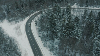 Aerial view of a winding snowy mountain road cutting through a dense winter forest. Mountain road...