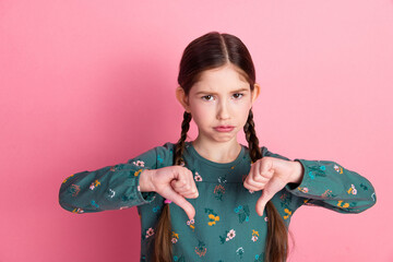 Young girl with braided hair making thumbs down gesture on pink background, expressing disapproval...