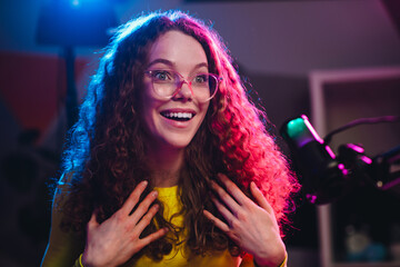 Young female streamer with curly hair enjoying online streaming in neon light studio