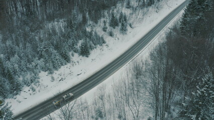 Aerial view of a winding snowy mountain road cutting through a dense winter forest. Mountain road...