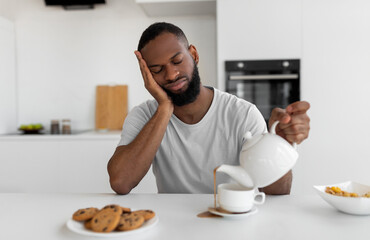 Lack Of Sleep Concept. Portrait of tired young African American man sleeping while sitting at...