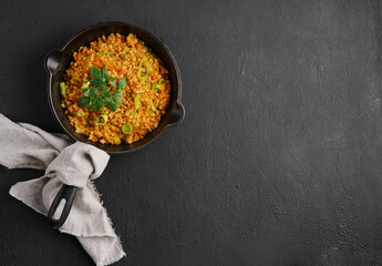 Black pan with dish from red lentil with leek on black background. Vegan cuisine. top view , copy space