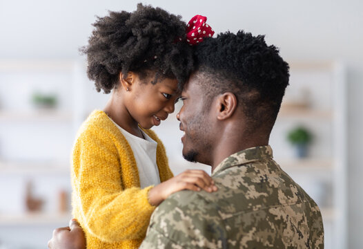 Portrait Of Black Cute Little Girl Embracing With Her Military Father, African American Male Soldier In Camouflage Uniform Cuddling His Daughter, Bonding With Female Child At Home, Side View, Closeup