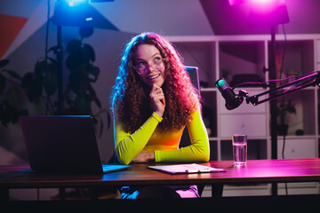Young woman in a neon-lit room hosting a live streaming session using a microphone and laptop