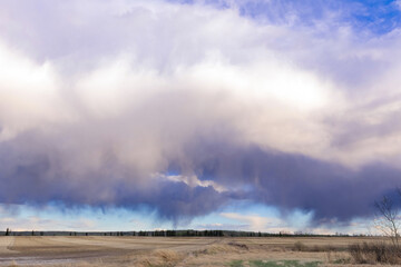 A scenic rural landscape capturing a freshly seeded agricultural field under a dramatic cloudy spring sky, raining in the horizon.
