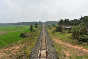 Long railway track extending into the horizon, flanked by green fields in Tripura.