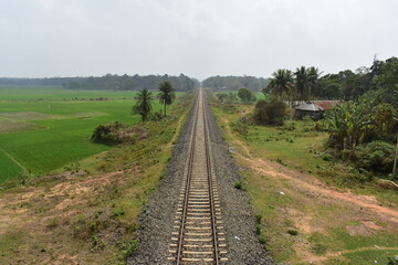Long railway track extending into the horizon, flanked by green fields in Tripura.
