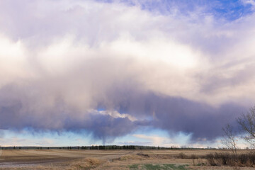 A scenic rural landscape capturing a freshly seeded agricultural field under a dramatic cloudy spring sky, raining in the horizon.