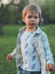 Close up of a young boy of 2 years standing on a green lawn