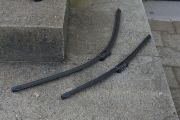 Two sleek, dark wiper blades rest on a textured concrete surface, highlighting their robust design and readiness for clear vision.