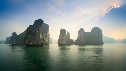 Naklejka premium Towering Sea Stacks in Emerald Ocean off Ha Long Bay, Vietnam – Morning Mist and Sun Rays Through Clouds, Scenic Seascape, Limestone Formations, Coastal Nature, Asian Landscape, Vietnam Travel