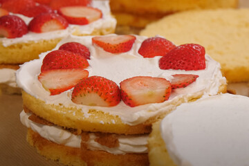 Partially assembled strawberry shortcake with whipped cream and fresh strawberries layered between sponge cake rounds on a kitchen surface

