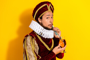 Young nobleman dressed in renaissance costume sipping drink with curly straw on yellow backdrop