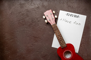 Small guitar ukulele on To do list with words Have fun. Musical instruments, top view