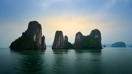 Naklejka premium Towering Sea Stacks in Emerald Ocean off Ha Long Bay, Vietnam – Morning Mist and Sun Rays Through Clouds, Scenic Seascape, Limestone Formations, Coastal Nature, Asian Landscape, Vietnam Travel