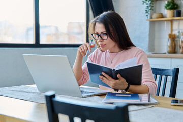 Middle-aged serious woman working at computer laptop in home office
