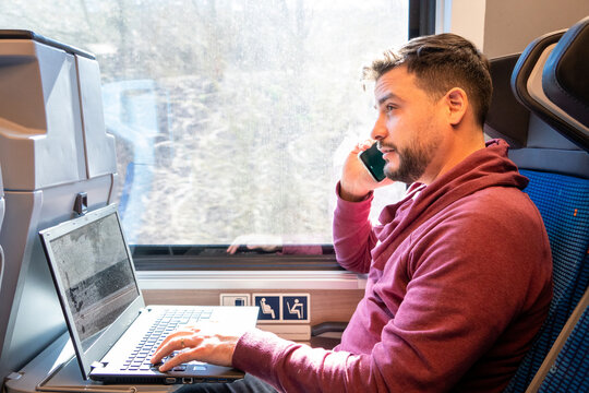 Hombre trabajando con su portatil y su teléfono en el tren mietras se desplaza a su destino