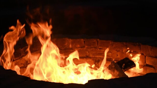 A mesmerizing slow-motion close-up of flames dancing in a fire pit at a luxury hotel during nighttime.