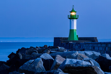 The green and white lighthouse in the harbor of Sassnitz on Rügen shines at dusk