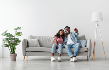 Weekend Leisure. Happy relaxed millennial black guy and lady watching tv in living room interior,...
