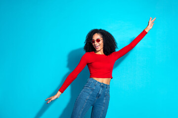 Joyful young woman in red top with curly hair expressing happiness against a vibrant blue background