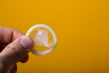 Hand holding a thin latex condom, close up, yellow background, sexual protection concept