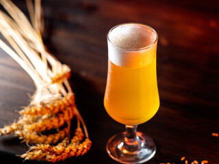 Cold beer glass on wooden table with wheat ears