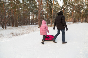 Father and daughter having fun with snow tube in the forest
