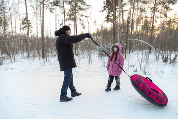Dad with his daughter walking with snow tubing in the winter forest