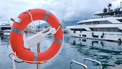 Orange lifebuoy on a metal stand near luxury yachts in a marina, Port Montenegro, with cloudy sky