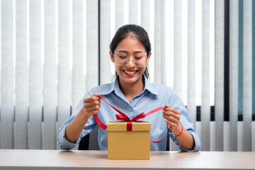 Happy woman is smiling and holding present box to wrapped with red ribbon while preparing gift for celebrate