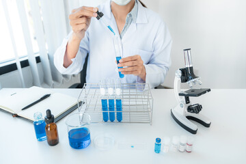 Fototapeta premium Scientist woman in protective face mask dropper to dropping blue liquid into test tube while working