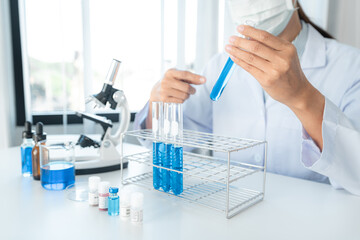 Scientist woman in medical face mask is experiment produce coronavirus vaccine and pointing on test tube