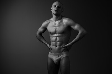 Fototapeta premium Athletic man posing confidently in black and white, showcasing strong physique with dramatic lighting, creating an impactful visual presence.