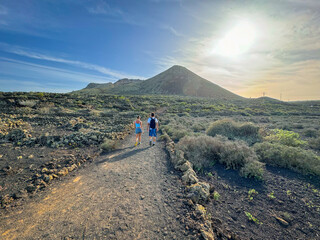 LENS FLARE: Couple walks along dusty path, heading towards a volcanic mountain, surrounded by dark,...