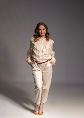 Fashion model posing in studio wearing white lace shirt and white pants