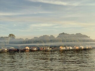 A fog settles over the river like a soft, pale veil, blurring the edges between water, sky, and...