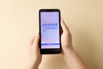 Menstruation. Woman holding smartphone with period calendar application on beige background, top...