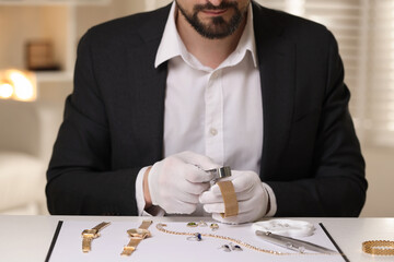 Appraiser with loupe evaluating luxury bracelet at table indoors, closeup