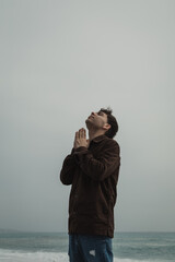 Man Praying With A Rosary And Eyes Closed On The Shore During Winter Stormy