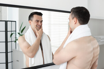 Smiling man after shaving looking at mirror in bathroom